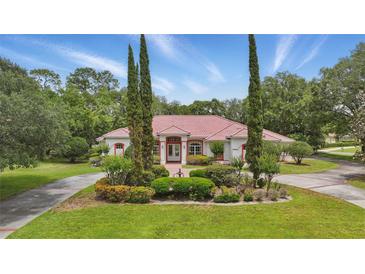 Charming single-story home featuring a vibrant red roof and lush landscaping, set against a backdrop of mature trees and blue skies at 1641 Timber Hills Dr, Deland, FL 32724