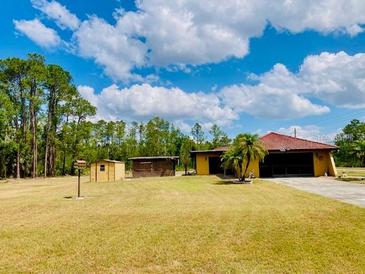 Expansive front yard with a single-story home, wooden storage units, and a backdrop of lush trees at 7380 Orange Ave, Indian Lake Estates, FL 33855