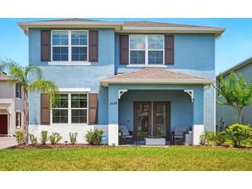 Charming two-story blue home featuring a covered front porch, lush landscaping, and beautiful architectural details at 3049 Meleto Blvd, New Smyrna Beach, FL 32168
