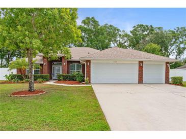 Charming brick home with a well-manicured lawn, mature trees, and a three car garage at 703 Elkhorn Fern Ln, Deland, FL 32720