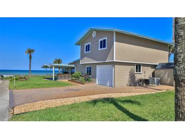 Beach home with a two-car garage, brick-paved driveway, grass lawn, and a covered outdoor entertainment area at 8 Ocean Dunes Dr, Ormond Beach, FL 32176