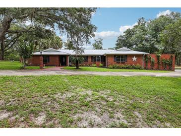 Charming one-story brick home featuring a metal roof, manicured lawn and mature trees at 2221 Oak Hill Dr, Deland, FL 32720