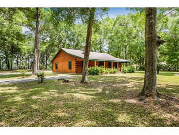 Charming log cabin home featuring a covered porch and surrounded by lush greenery at 2955 Se 156Th Place Rd, Summerfield, FL 34491