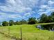 Scenic view of a pond with a grassy bank, trees, and blue sky, enhanced by a rustic fence at 850 Eden Dr, Saint Cloud, FL 34771