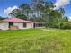 Backyard view of the home with a red roof, set on a large lot with tall grass at 318 Mitnik Dr, Deltona, FL 32738