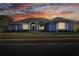 Charming blue home with picturesque sunset backdrop, beautiful landscaping, and well-lit windows at 5810 Lake Victoria Dr, Lakeland, FL 33813