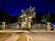 Elegant community entrance featuring a decorative gate, well-lit palm tree, and manicured landscaping at 1568 Cordgrass Way, Lakeland, FL 33813
