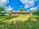 A well-kept lawn and the rear exterior of a brown home under a bright blue sky with scattered clouds at 1119 Indigo Rd, Ormond Beach, FL 32174
