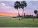 Picturesque backyard boasts vibrant green lawn, waterfront view, and swaying palm trees against a sunset sky at 64 Ocean Palm S Dr # 64, Flagler Beach, FL 32136