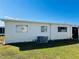 Rear exterior view showing a single wide mobile home with AC unit and grassy lawn at 215 Rue De Paresse, Tavares, FL 32778