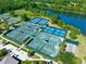 Aerial view of multiple tennis courts, bocce ball court and lush landscaping by a serene lake at 820 Aldenham Ln, Ormond Beach, FL 32174