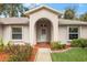 Charming home entrance with an arched doorway, tiled path, and well-maintained landscaping at 66 Old Sunbeam Dr, South Daytona, FL 32119