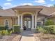 Elegant home foyer features large glass front doors, tiled floor, with white columns and green manicured bushes at 22527 Lake Seneca Rd, Eustis, FL 32736