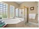 Bright bathroom featuring a soaking tub with shower, tile surround, glass block window and bronze fixtures at 3428 Rexford Cir, Ormond Beach, FL 32174