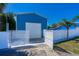 View through the white gates shows a modern workshop and a glimpse of the charming blue home at 318 Eastwood Dr, Daytona Beach, FL 32118