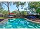 Sparkling swimming pool with a lounge area, umbrella-covered table, and beautiful trees for shade at 35 Whippoorwill Ln, Ormond Beach, FL 32174