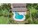 Aerial view of a kidney-shaped pool with steps and an umbrella, surrounded by lush greenery and a fenced yard at 428 Pelican Bay Dr, Daytona Beach, FL 32119