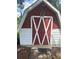 Well-kept red and white shed exterior with white trim, a decorative leaf accent, and a clean brick walkway at 1218 Daytona Ave, Daytona Beach, FL 32117