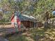 Two-story red home with a metal roof surrounded by mature trees and lush foliage creating a tranquil setting at 13524 Corkwood Ln, Astatula, FL 34705