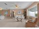 Comfortable living room with neutral walls and carpet, featuring a ceiling fan and natural light from a large window at 17574 Se 106Th Ave, Summerfield, FL 34491