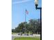 Community entrance with an American flag, landscaped roundabout, streetlights, and mature trees at 5206 Fantasy Way, Leesburg, FL 34748