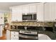 Kitchen featuring white cabinets, stainless steel microwave, granite countertops, and mosaic backsplash at 1405 Hilltop Dr, Mount Dora, FL 32757