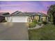 Two-story house exterior with a two car garage, landscaping, and warm lighting at 1315 Greenville Way, The Villages, FL 32162