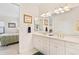 Bright bathroom featuring double sinks, white cabinets, gold hardware, and a view to the bedroom at 38230 Yale Cir, Leesburg, FL 34788