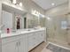 Bright bathroom featuring double vanity with white cabinets, large mirror, and glass-enclosed shower with neutral tile at 955 Ladera Ranch Rd, Kissimmee, FL 34759