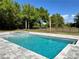 Sparkling blue swimming pool with a stone patio and black metal fence, surrounded by lush greenery and trees at 16914 Vinci Way, Bella Collina, FL 34756