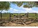 Wooden gate opens to a green pasture under a blue sky with scattered clouds at 5415 Banana Point Dr, Okahumpka, FL 34762
