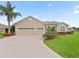 Tan two-story house with a three-car garage and lush landscaping at 12205 Se 174Th Pl, Summerfield, FL 34491