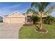 Tan house with three-car garage, lush landscaping, and palm trees at 3113 Sweetgum St, The Villages, FL 32163