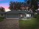 House exterior at dusk showcasing stone accents, screened garage, and landscaping at 5004 Saint Andrews Arc, Leesburg, FL 34748