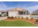 Tan house with white picket fence, two-car garage, and screened porch at 1387 Zest Ave, The Villages, FL 32163