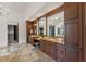 Elegant bathroom featuring granite counters, dual sinks, and beautiful brown wood cabinets and trim at 15118 Pendio Dr, Bella Collina, FL 34756