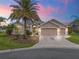 Tan three-car garage home with palm trees and landscaped yard at sunset at 1644 Shell Point Ave, The Villages, FL 32162