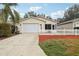 Front view of a tan house with a white picket fence and a two-car garage at 17461 Se 93Rd Retford Ter, The Villages, FL 32162