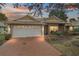 Tan one-story house with white garage door, brick driveway, and landscaping at 791 Princeton Dr, Clermont, FL 34711