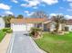 Charming single-Gathering home featuring an attached two car garage, landscaping, and an inviting front yard with palm tree accents at 17412 Se 76Th Flintlock Ter, The Villages, FL 32162