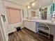 Bathroom vanity with white cabinetry, wood-look floors, and pink window blinds at 114 Chestnut St, Leesburg, FL 34748