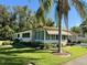 Tan mobile home with corner lot, lush landscaping, and palm trees at 114 Chestnut St, Leesburg, FL 34748