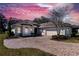 Inviting home exterior featuring a brick driveway and professional landscaping against a pink and purple sky at 5312 Meadow Hill Loop, Lady Lake, FL 32159