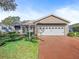 Tan one-story house with white garage door and landscaped lawn at 1711 Lilly Ln, The Villages, FL 32159