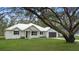 White farmhouse exterior with metal roof, landscaping, and large tree at 18315 Dells Cv, Groveland, FL 34736