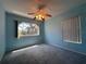 Bedroom featuring blue walls, carpet, ceiling fan, and bright windows overlooking the outdoor landscaping at 5095 China Sea Dr, Tavares, FL 32778