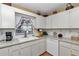 Well-lit kitchen sink area with white cabinets, decorative wallpaper, and window with floral curtains and blinds at 8862 Sw 92Nd St # D, Ocala, FL 34481
