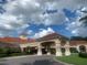 Clubhouse exterior view showcasing the porte cochere, terra cotta roof and lush landscaping under a cloudy sky at 3782 Avon Ct, Clermont, FL 34711