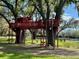 Red wooden treehouse with ladder and deck, perfect for outdoor play and relaxation at 415 Carman Dr, Leesburg, FL 34748