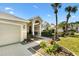 Close-up of the front entrance with an arched entryway, flower garden, and three-car garage at 1840 Madero Dr, The Villages, FL 32159